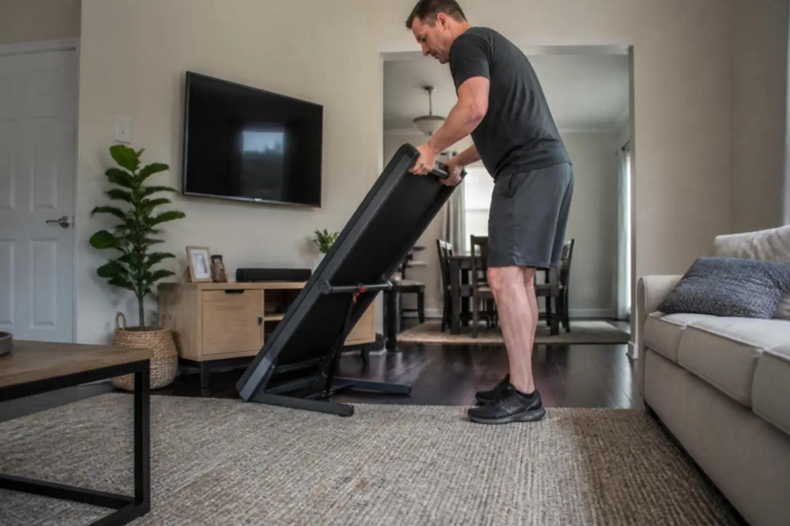 Man folding a compact treadmill in a small living room