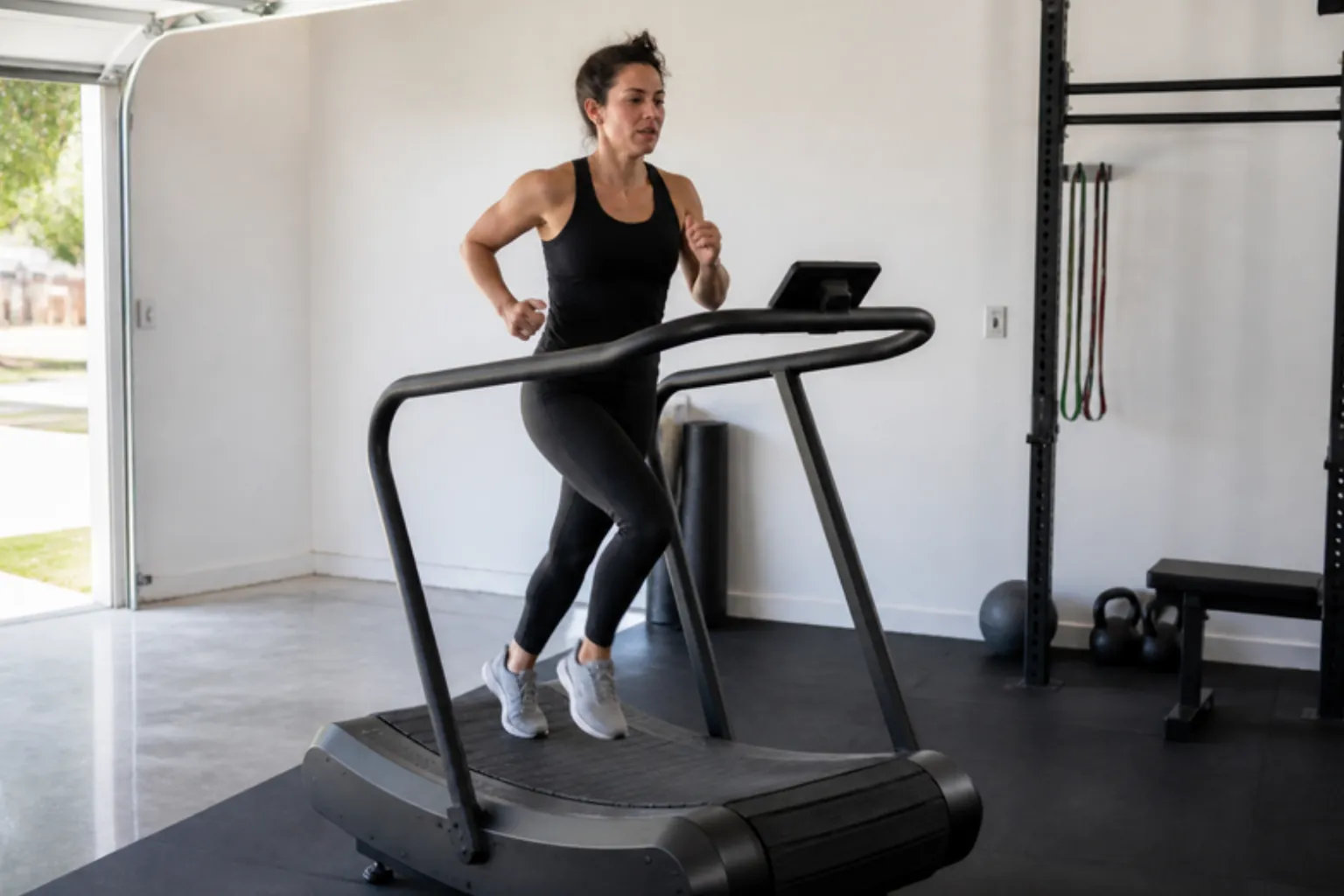 Woman running at pace on a curved treadmill in a garage gym