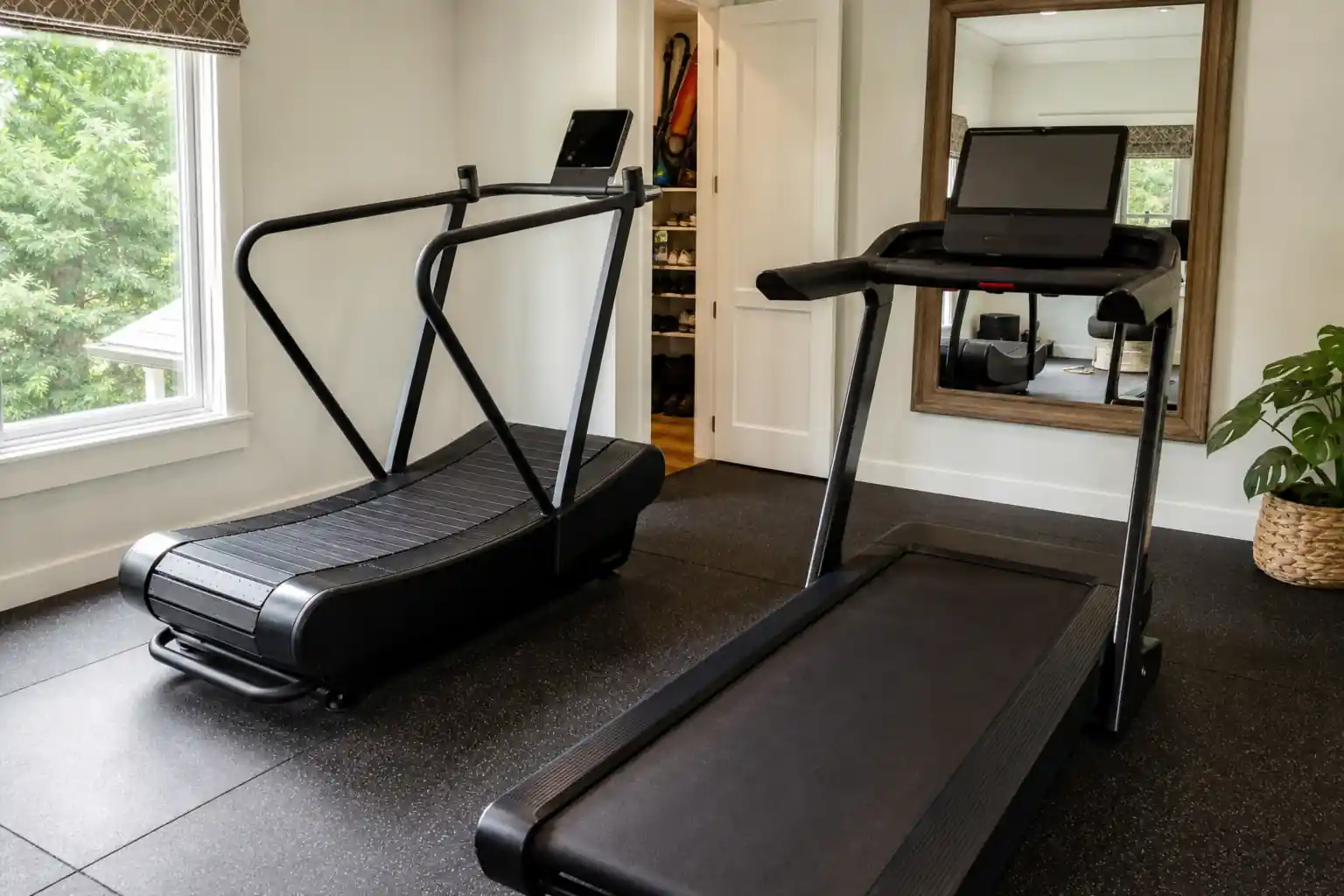 Curved vs flat treadmill: a home gym with a black self-powered curved slat treadmill next to a black flat motorized treadmill with a console, rubber f